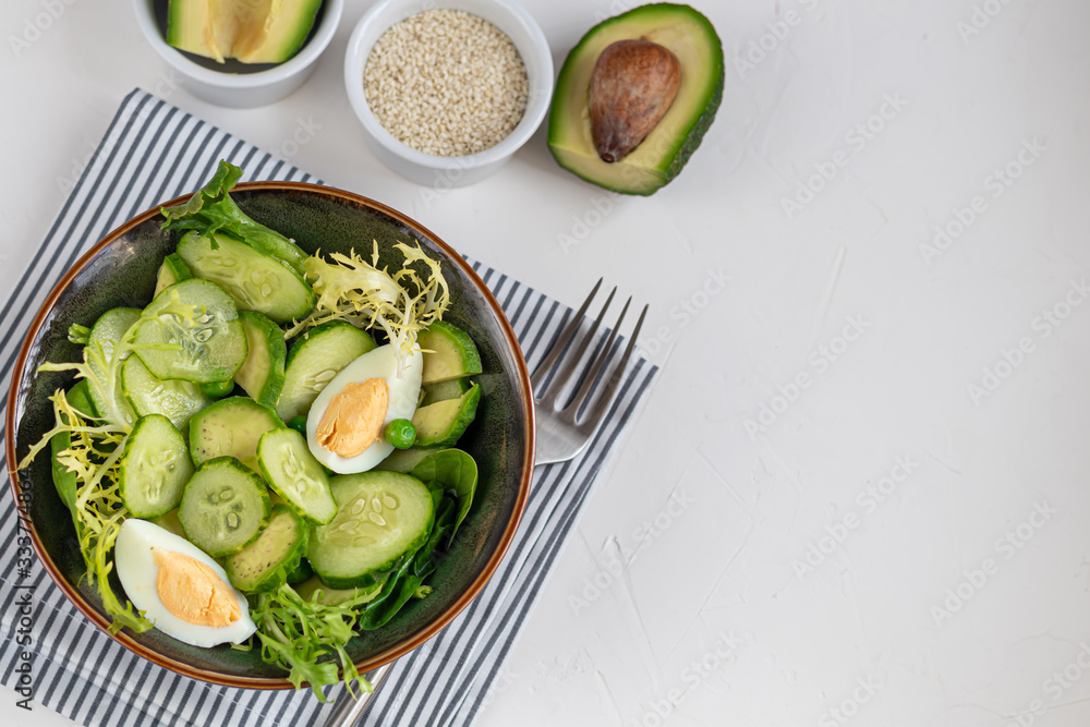 Salad of fresh cucumbers, spinach leaves, arugula, avocado. Served with slices of eggs and red pepper. Dietary nutrition. Breakfast for the whole family. Vitamin plate. On a light background. Salad of fresh cucumbers, spinach leaves, arugula, avocado. Served with slices of eggs and red pepper. Dietary nutrition. Breakfast for the whole family. Vitamin plate. On a light background.