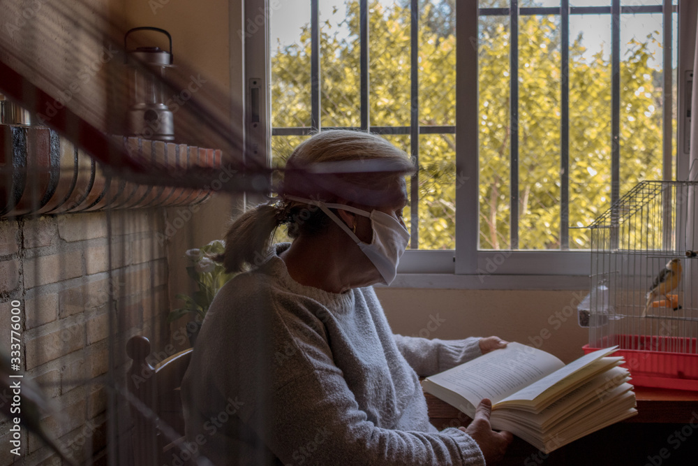 Mujer con mascarilla leyendo un libro en su casa mientras pasa la cuarentena
