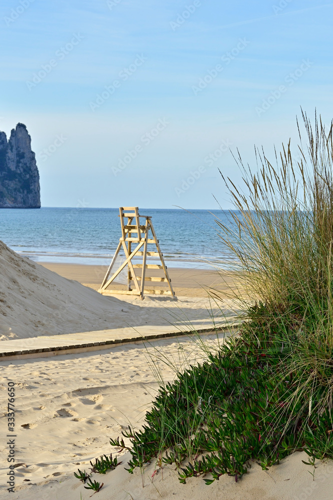 Empty lifeguard chair on an empty beach with beach plants and cliffs at the horizon