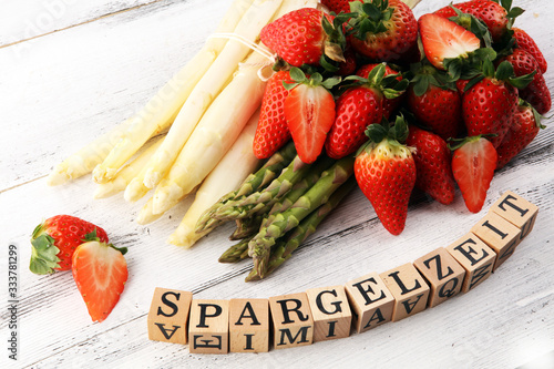 White and green asparagus with strawberries on rustic background with Spargelzeit wooden letter.