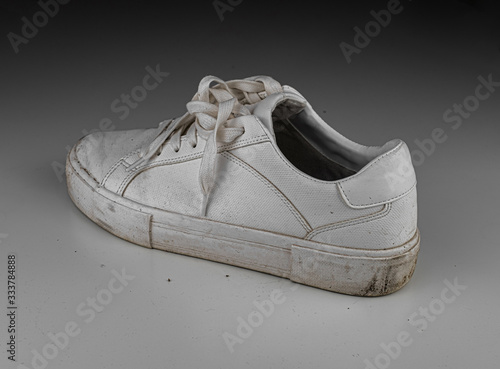 Dirty, used, muddy white left shoes on white dirty floor