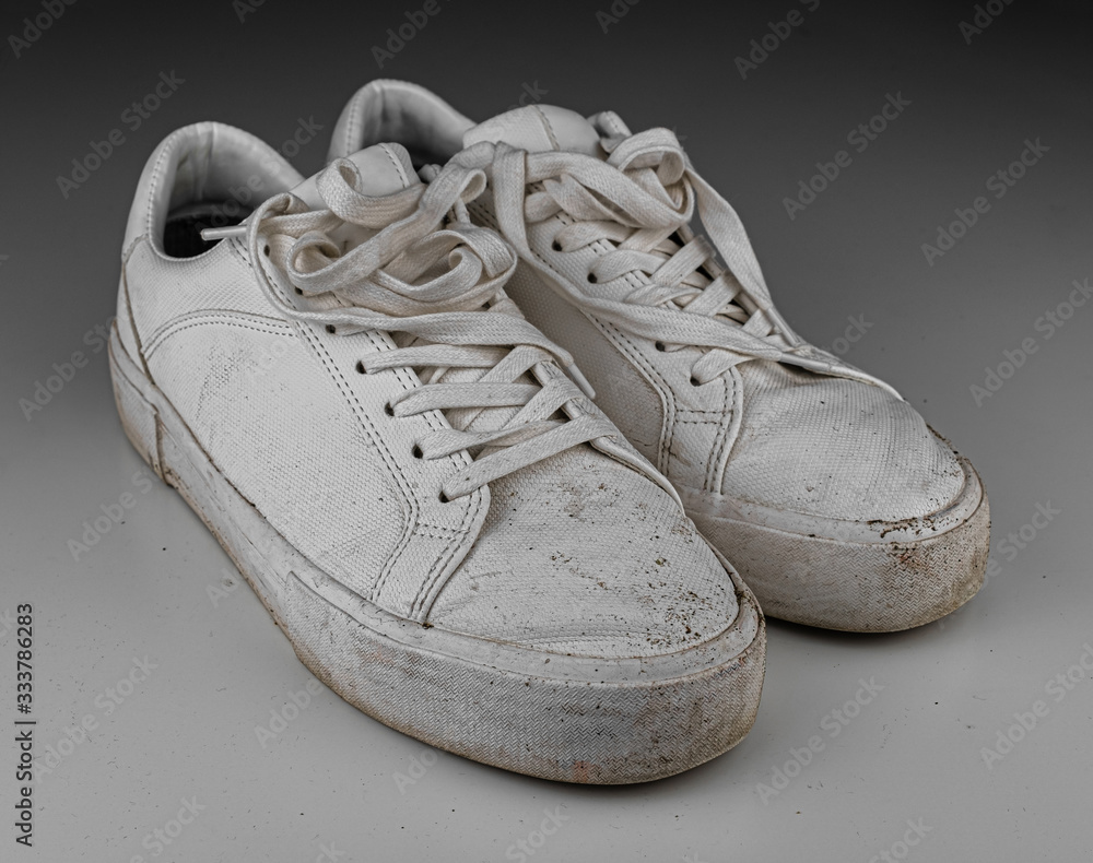 Dirty, used, muddy white dirty pair of shoes on white dirty floor