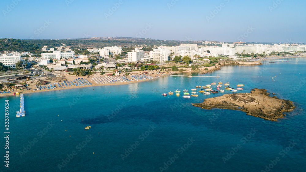 Aerial bird's eye view of Fig tree bay in Protaras, Paralimni, Famagusta, Cyprus. Tourist attraction golden sandy beach with boats, sunbeds, sea restaurants, water sports on summer holidays from above