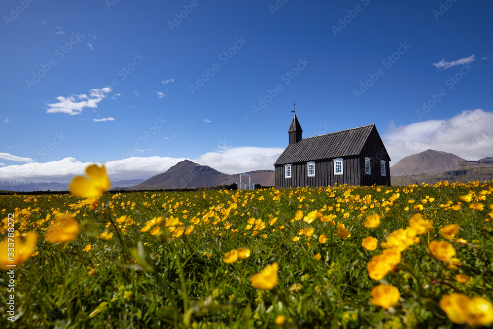 Black wooden church Budakirkja at Snaefellsnes peninsula, Budir village, Western Iceland, Europe. Summer landscape with chapel, mountains and flowers. Famous landmark. Travelling concept background.