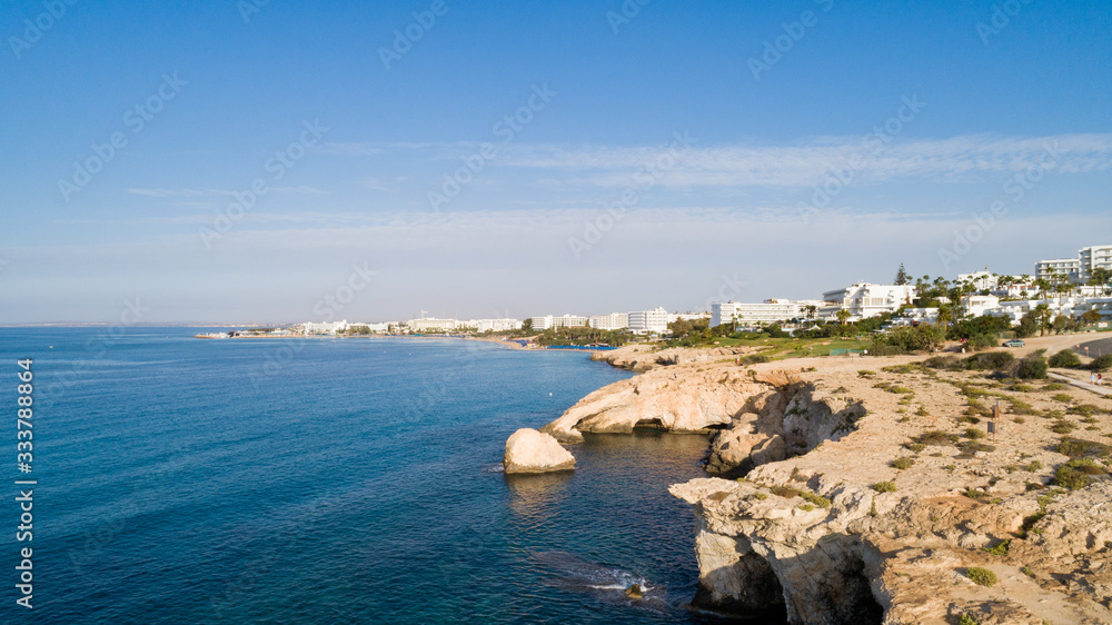 Fototapeta premium Aerial bird's eye view of coastline landmark ‘Love bridge’ and sea caves at Cavo Greco, Ayia Napa, Famagusta, Cyprus from above. A tourist attraction cliff rock natural formation arch in Ammochostos.