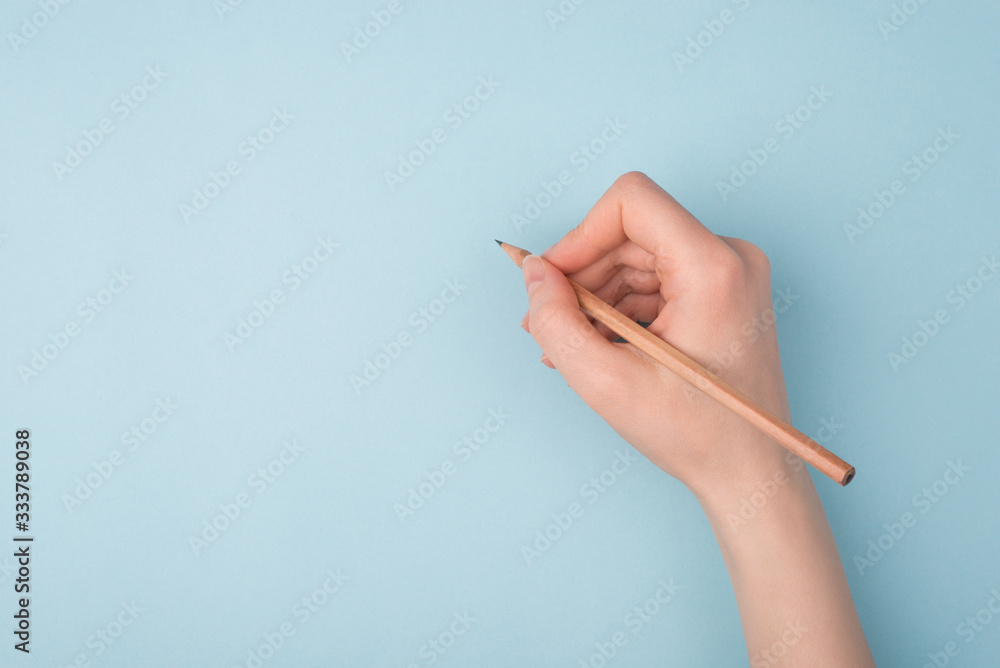 © ActionGP - Top close up pov above overhead view photo of hand holding wooden pencil starting to draw a picture isolated over blue pastel color background