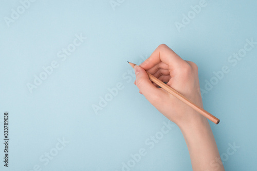 Top close up pov above overhead view photo of hand holding wooden pencil starting to draw a picture isolated over blue pastel color background photo