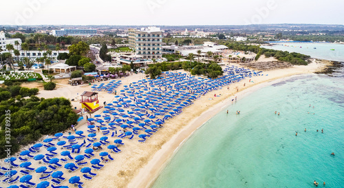 Aerial bird's eye view of famous Makronissos beach coastline, Ayia Napa, Famagusta, Cyprus. Landmark sea tourist attraction Makronisos bay at sunset with golden sand, sunbeds in Agia Napa from above.