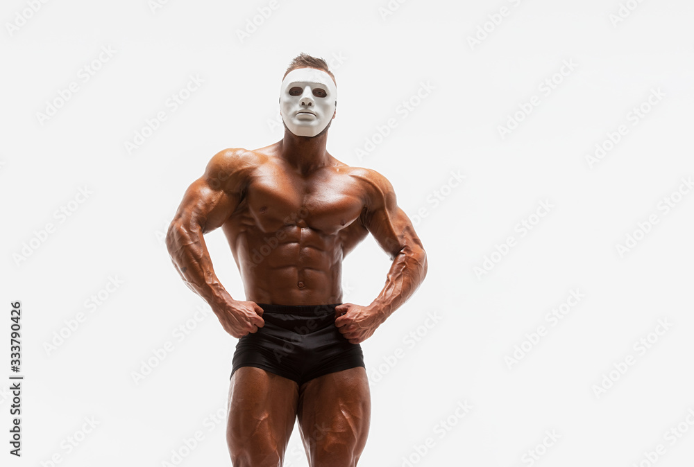 Mysterious Muscular man hiding behind white mask Flexing Muscles. Bodybuilder with white mask on his face posing. Studio shot on white background Mysterious Muscular man hiding behind white mask Flexing Muscles. Bodybuilder with white mask on his face posing. Studio shot on white background