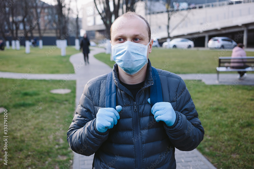 The portrait of sad man in blue surgical mask and gloves walked on the street. Pandemic coronavirus 2020. Quarantine.Virus concept. Epidemic infection. The portrait of sad man in blue surgical mask and gloves walked on the street. Pandemic coronavirus 2020. Quarantine.Virus concept. Epidemic infection.