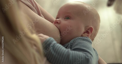 Portrait of cute baby sucking mom's breasts and looking at camera
