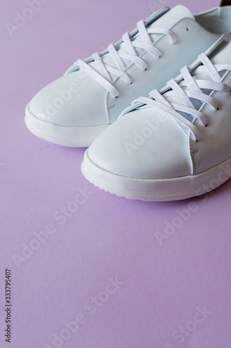 A pair of white sneakers on purple background. Copy space.