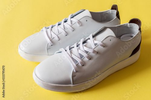 A pair of white leather sneakers on yellow background. Copy space.