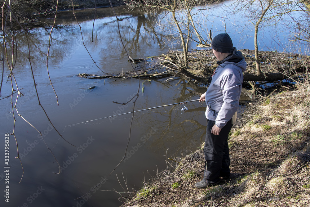 A male fisherman fishing in the spring with a fishing rod from the Bank on the river. Sunny day, spring landscape.