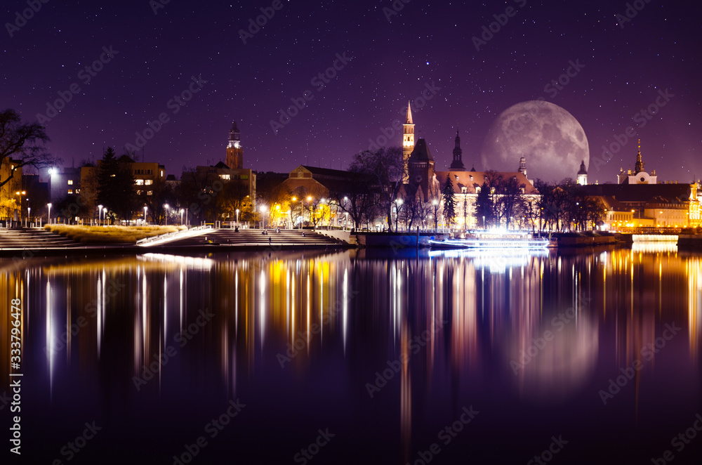 Fantastic sky with huge moon over Wroclaw City, Odra river and reflections of historical buildings in it.