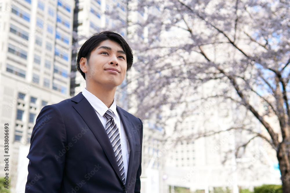 オフィス街の桜を背景に笑顔で立つ日本人男性ビジネスマン