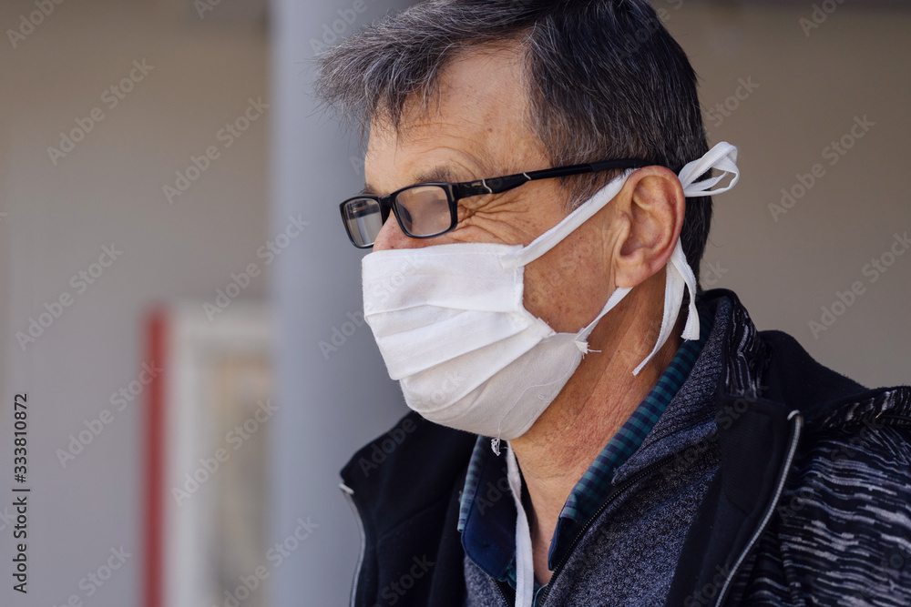 Side view portrait of caucasian senior man standing outdoor in front of the building or home wearing medical protective mask to prevent pandemic disease spread protecting from viruses pollution in day Side view portrait of caucasian senior man standing outdoor in front of the building or home wearing medical protective mask to prevent pandemic disease spread protecting from viruses pollution in day