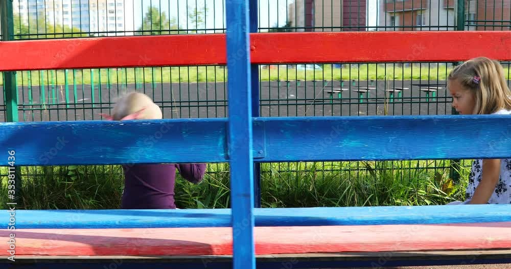 two happy little girls play on a bench in the yard. two happy little girls play on a bench in the yard.