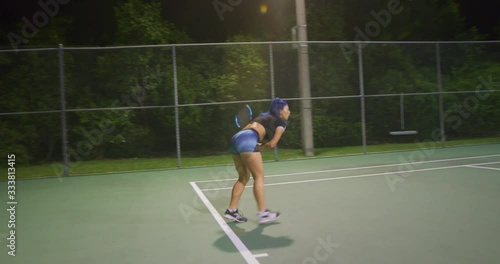 Woman serving tennis ball at night