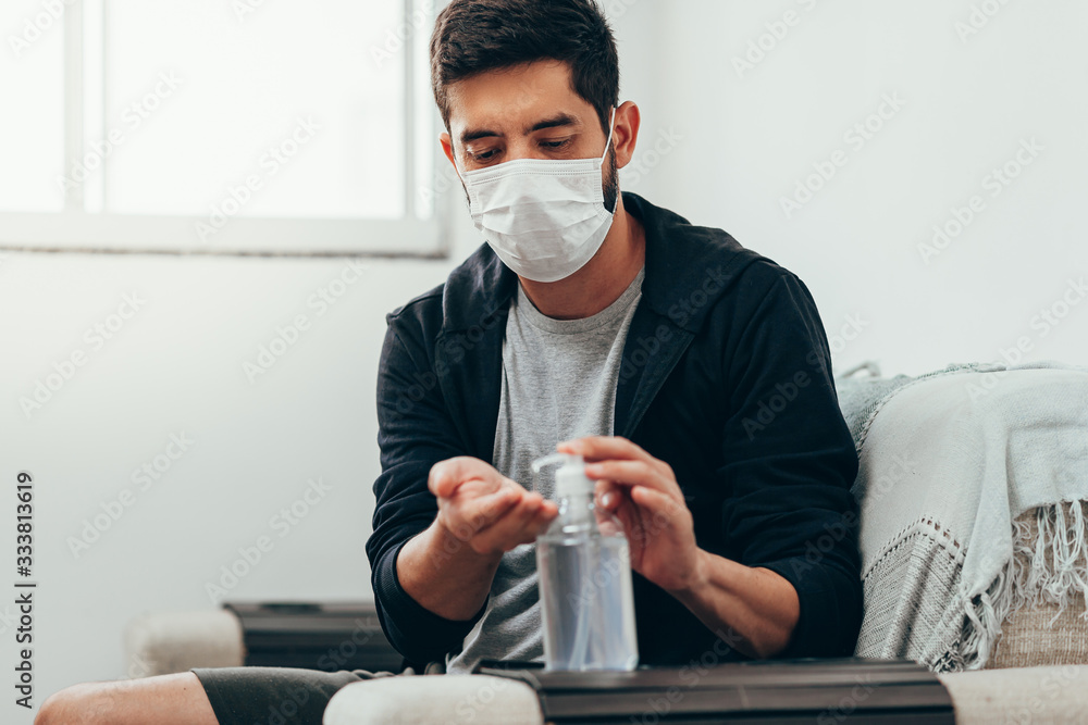 Coronavirus. Man in quarantine wearing protective mask sanitizing his hands with alcohol gel