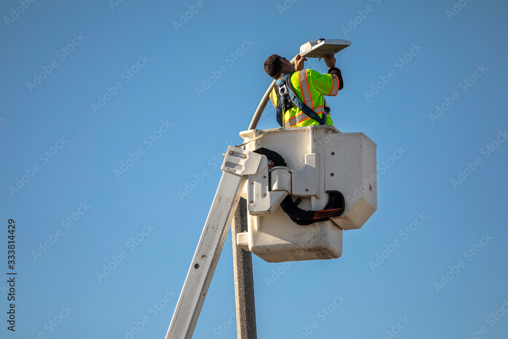 Man in manlift bucket repairing street light against blue sky Man in manlift bucket repairing street light against blue sky