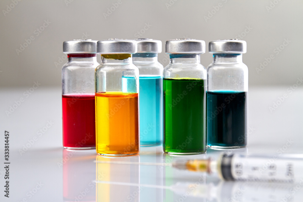 Glass vials with colored medicine liquid and syringe. White reflective surface. Glass vials with colored medicine liquid and syringe. White reflective surface.