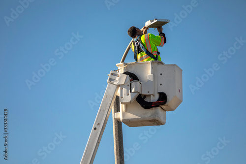 Man in manlift bucket repairing street light against blue sky photo