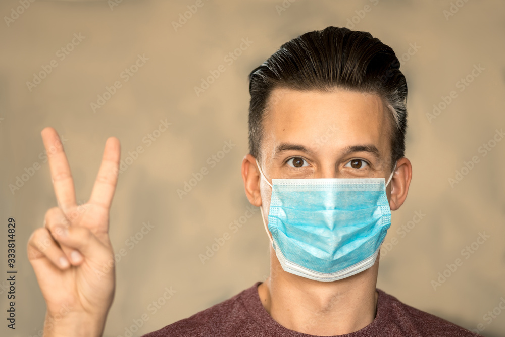 Theme of coronavirus and safety. A young man in a blue mask from a virus shows PEACE. Horizontal frame Theme of coronavirus and safety. A young man in a blue mask from a virus shows PEACE. Horizontal frame