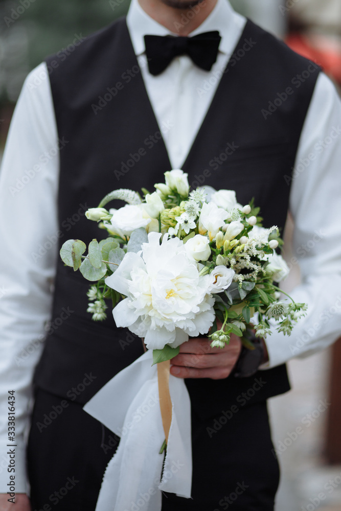 Wedding bouquet of white delicate beautiful in the hands of the groom in a black suit Wedding bouquet of white delicate beautiful in the hands of the groom in a black suit