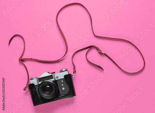 Vintage retro film camera in leather cover with strap on pink background. Top view