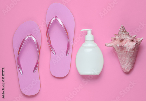 Beach accessories. Fashionable beach pink flip flops, sunblock bottle, seashell on pink paper background. Flat lay. Top view