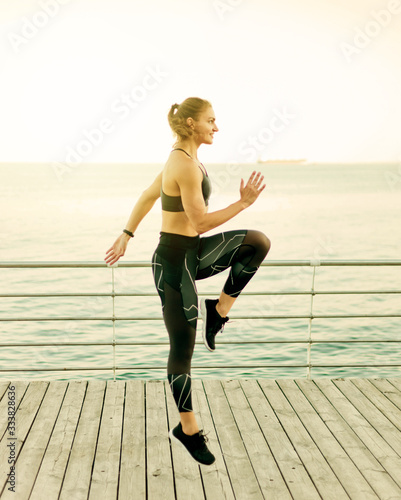 Young fit woman in sportswear doing a high jump on a beach terrace against the sea. Outdoor Sports Concept