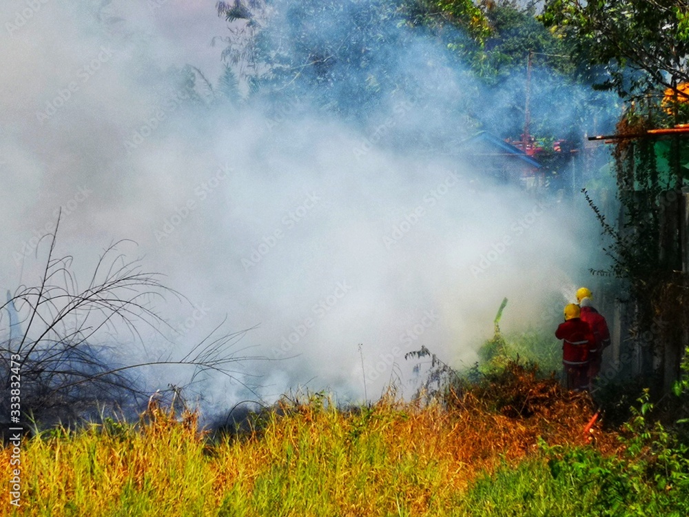 Fototapeta premium Fireman using water and extinguisher to fighting with fire flame in an emergency situation.,There is dirty smoke floating over the area.