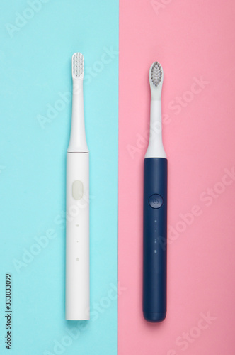 Two Modern electric toothbrushes on blue pink pastel background. Top view. Teeth care. Minimalism