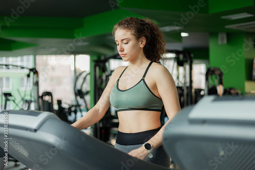 Young fit woman in sportswear before basic training runs on a treadmill in the gym. The concept of a healthy lifestyle, warming up, fitness.