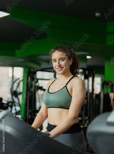Young fit woman in sportswear looking at camera on a treadmill in the gym. The concept of a healthy lifestyle, warming up, fitness.