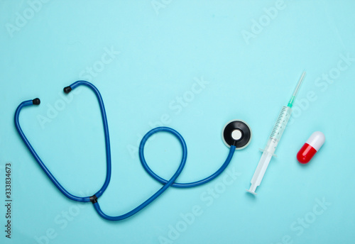 Flat lay medicine composition. Pill capsule, stethoscope, syringe with vaccine on a blue pastel background. Top view