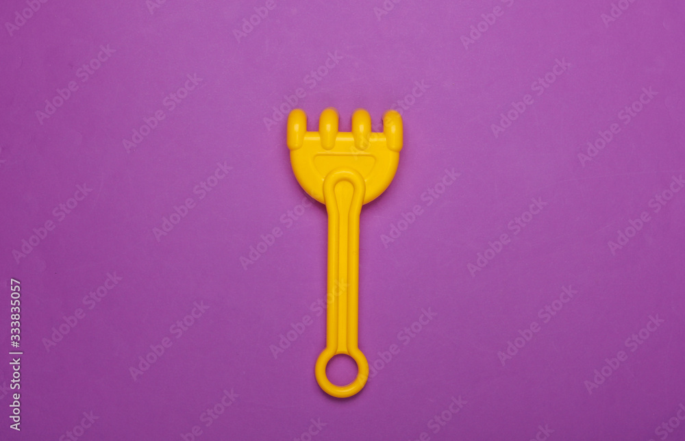 Children's rake for a sandbox or a beach on purple studio background. Top view Children's rake for a sandbox or a beach on purple studio background. Top view