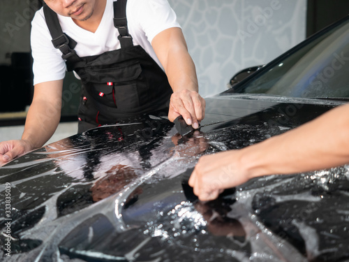 Car wrapping specialist putting vinyl foil or film on car. Car service worker install protective transparent film at the detailing vehicle workshop. Car paint protection with special film concept.