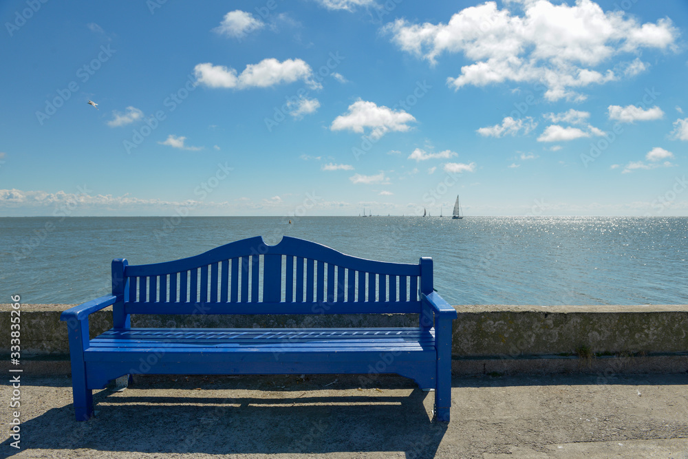 Blue wooden bench against the sea and yacht on the horizon.