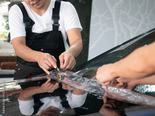 Car wrapping specialist putting vinyl foil or film on car. Car service worker install protective transparent film at the detailing vehicle workshop. Car paint protection with special film concept.