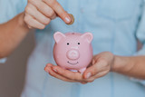female hands hold a pink piggy bank and puts a coin there. The concept of saving money or savings, investment