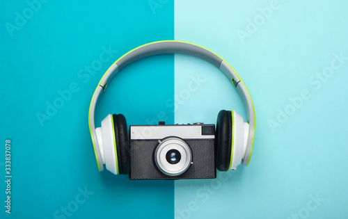 Stylish stereo headphones with retro camera on blue background. Music lover. Travel concept. Retro 80s. Top view.