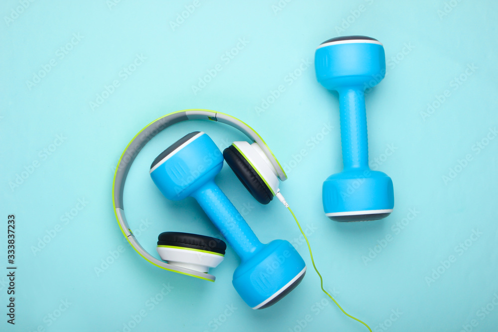 Flat lay sports and fitness composition. Dumbbells, headphones on blue background. Top view