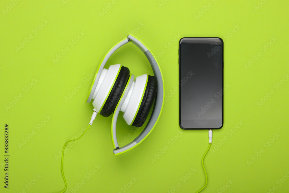 Portable folding stereo headphones with smartphone on green background. Music lover. Modern gadgets. Top view. Minimalism Portable folding stereo headphones with smartphone on green background. Music lover. Modern gadgets. Top view. Minimalism