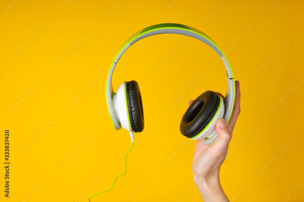 Hand holding stereo headphones on a yellow background. Hand holding stereo headphones on a yellow background.
