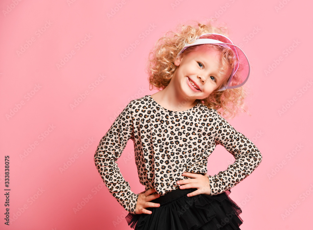 Portrait of playful blonde curly kid girl in leopard print sweatshirt, black skirt and fashion visor cap dancing Portrait of playful blonde curly kid girl in leopard print sweatshirt, black skirt and fashion visor cap dancing