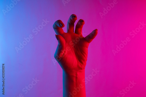 Halloween concept. Female hand with scary gestures. Neon blue-pink gradient light. Night glow. Creative art