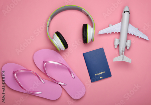 Travel concept. Headphones, airplane figurine, passport, flip flops on a pink pastel background. Flight voyage, trip, journey design. Beach vacation. Flat lay composition. Top view