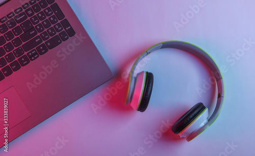 DJ or gaming concept. Laptop and headphones with neon blue-pink light. Top view photo